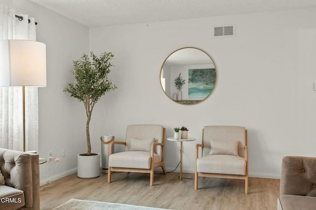 living area with visible vents, a textured ceiling, baseboards, and wood finished floors