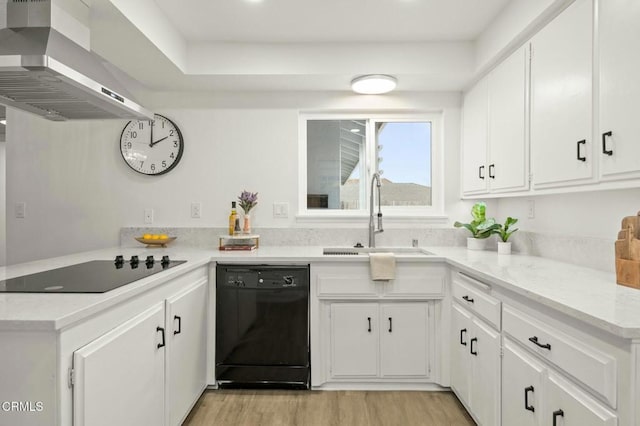 kitchen featuring black appliances, wall chimney range hood, light wood-style flooring, white cabinetry, and a sink