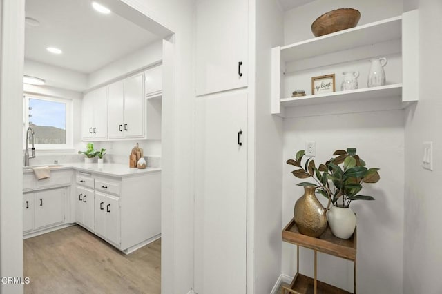 kitchen with light wood-type flooring, a sink, open shelves, white cabinetry, and light countertops