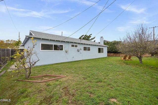 rear view of property with stucco siding, a chimney, a yard, and fence