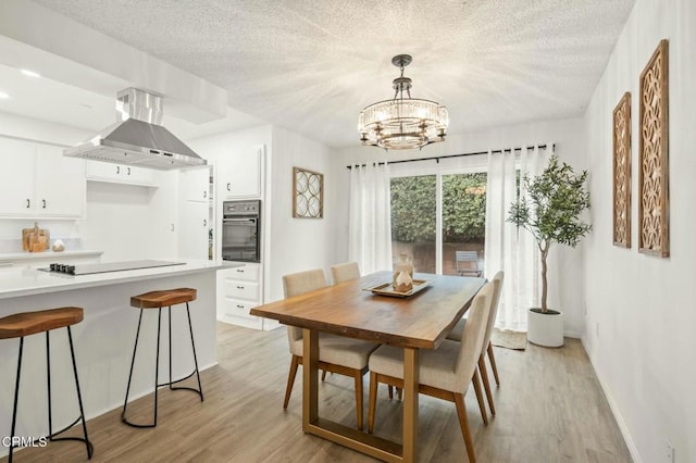 dining area with a notable chandelier, light wood finished floors, and a textured ceiling