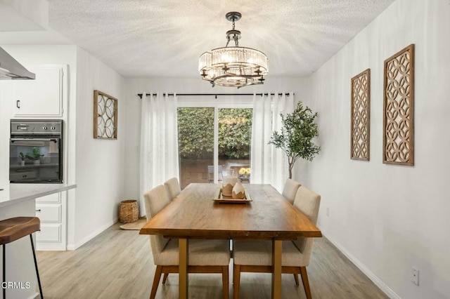 dining space featuring light wood-style floors, baseboards, a chandelier, and a textured ceiling