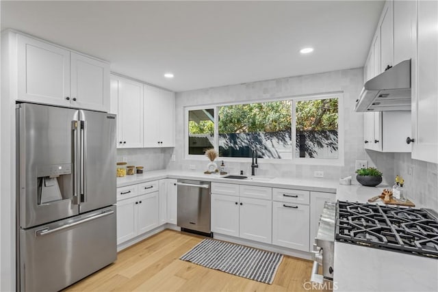 kitchen featuring light wood-style flooring, under cabinet range hood, stainless steel appliances, a sink, and white cabinetry