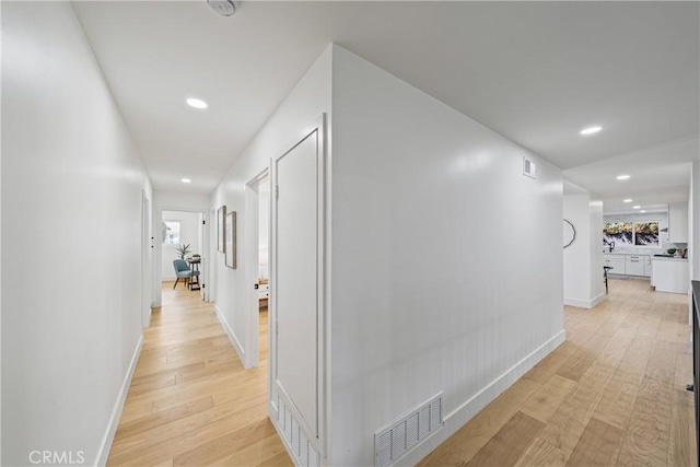 corridor featuring baseboards, visible vents, and light wood finished floors