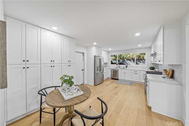 kitchen with white cabinets, under cabinet range hood, light wood finished floors, and high quality appliances