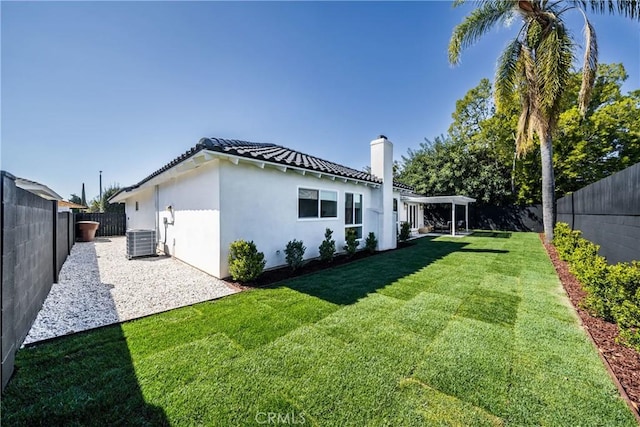 rear view of property with a fenced backyard, a tile roof, a yard, central AC, and stucco siding