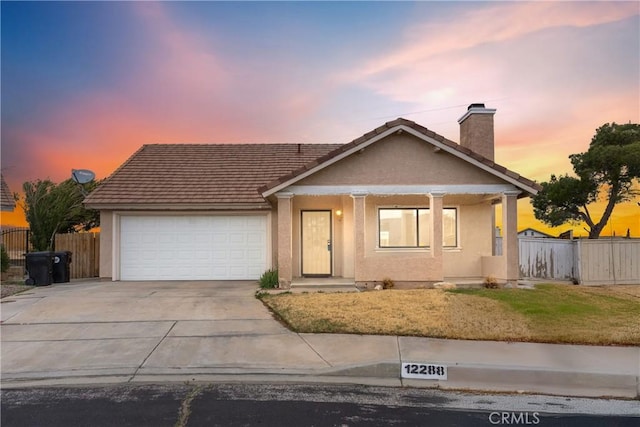 view of front of house featuring a chimney, stucco siding, concrete driveway, fence, and a garage