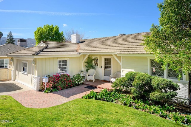 ranch-style home featuring board and batten siding, brick siding, a chimney, and a front lawn