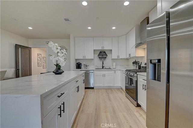 kitchen with visible vents, appliances with stainless steel finishes, a sink, light wood-type flooring, and wall chimney exhaust hood