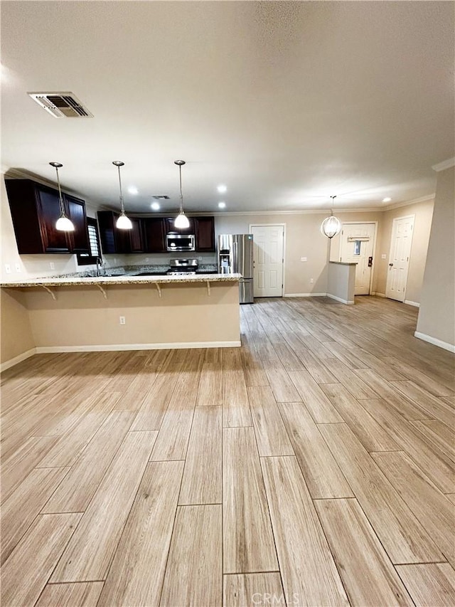 kitchen featuring visible vents, appliances with stainless steel finishes, a kitchen breakfast bar, light stone counters, and wood finish floors