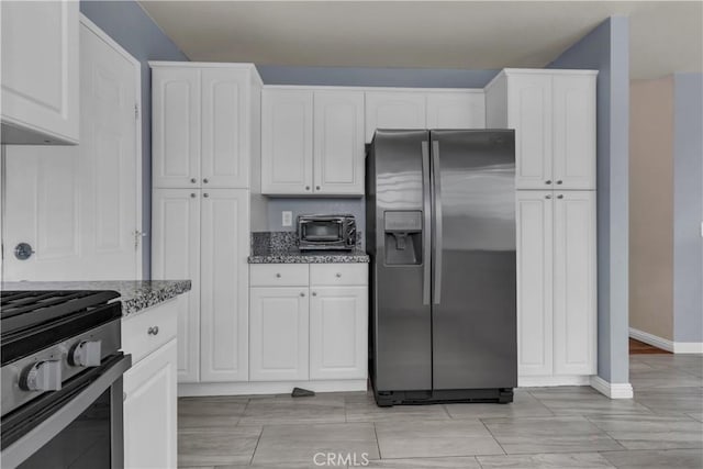 kitchen featuring appliances with stainless steel finishes, white cabinets, a toaster, stone counters, and baseboards