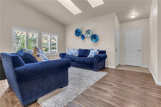 living room with lofted ceiling with skylight, light wood-type flooring, and baseboards