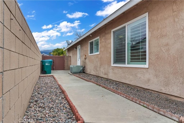 view of side of property featuring stucco siding, a patio area, cooling unit, and fence