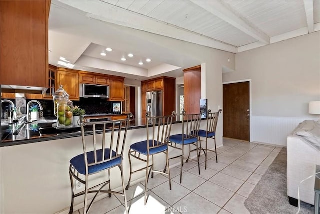 kitchen featuring a peninsula, appliances with stainless steel finishes, wainscoting, dark countertops, and a raised ceiling