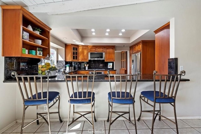 kitchen with a peninsula, appliances with stainless steel finishes, a tray ceiling, and tasteful backsplash