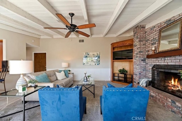 living area featuring a fireplace, visible vents, wainscoting, ceiling fan, and beamed ceiling