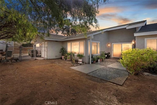 back of house at dusk with central AC unit, a gate, fence, a patio area, and stucco siding