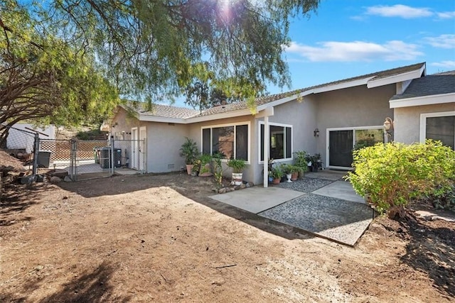 view of front of property with a patio, stucco siding, a gate, central AC, and fence