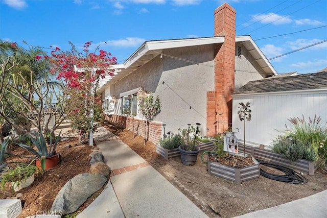 view of home's exterior featuring roof with shingles, a chimney, a vegetable garden, and stucco siding