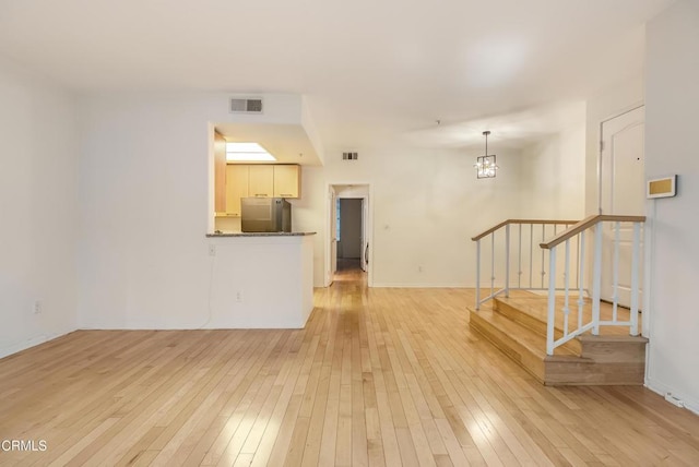 unfurnished living room with visible vents, a notable chandelier, stairs, and light wood finished floors