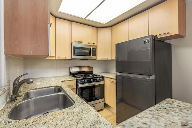 kitchen featuring light brown cabinetry, a sink, light stone counters, appliances with stainless steel finishes, and decorative backsplash