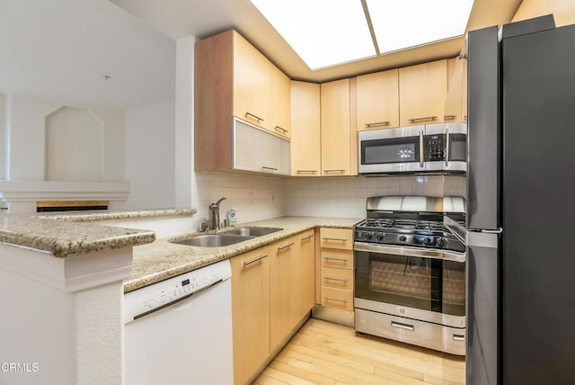 kitchen featuring light wood finished floors, light brown cabinetry, decorative backsplash, stainless steel appliances, and a sink