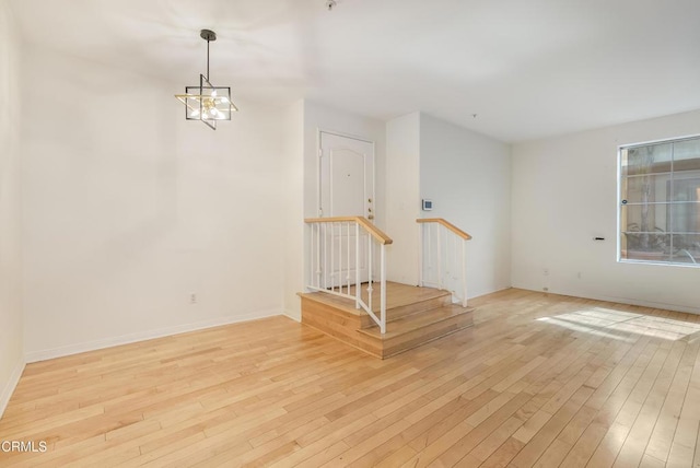 spare room with a notable chandelier, baseboards, and light wood-style floors