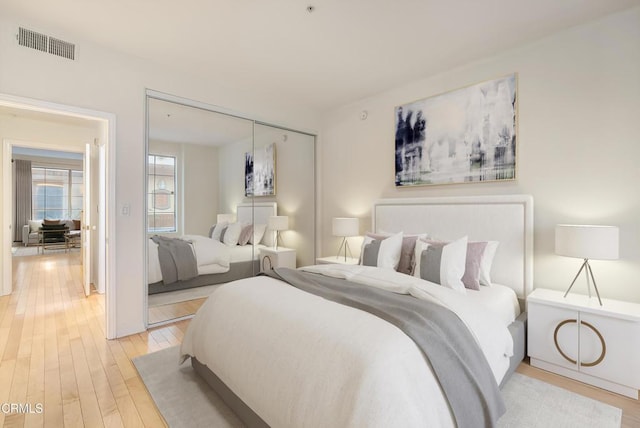 bedroom with visible vents, light wood-style floors, and a closet