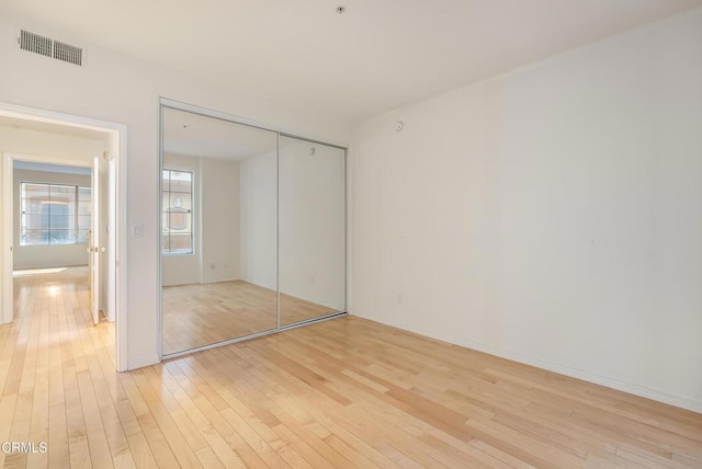 unfurnished bedroom with light wood-type flooring, visible vents, and a closet