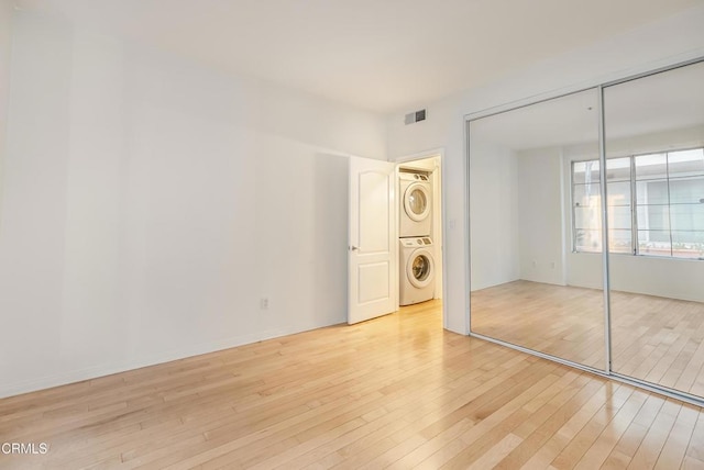 unfurnished bedroom with a closet, visible vents, light wood-style flooring, and stacked washer / drying machine