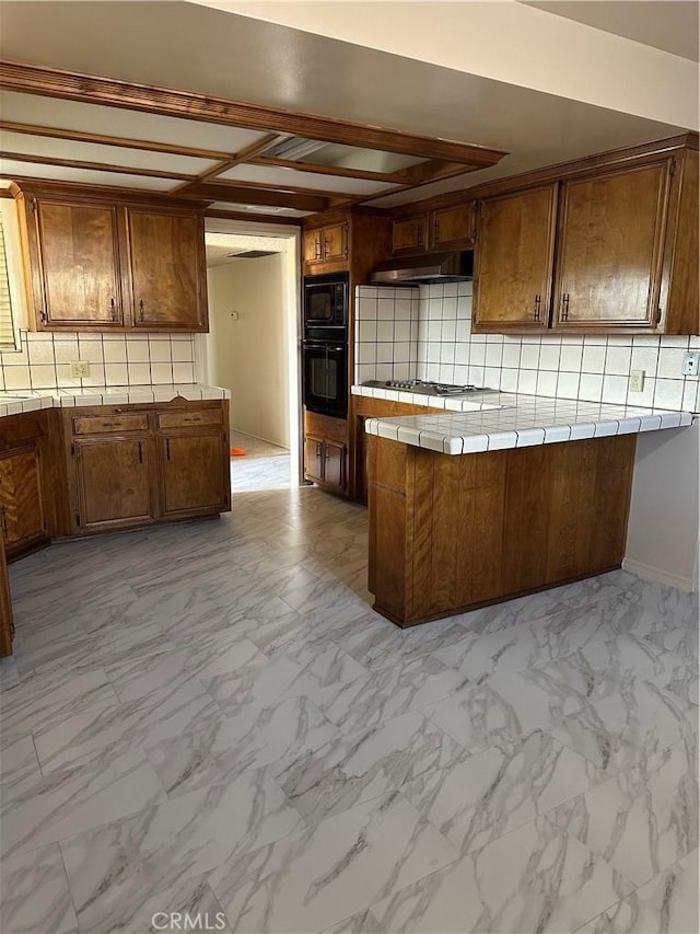 kitchen with black appliances, under cabinet range hood, tile counters, and marble finish floor