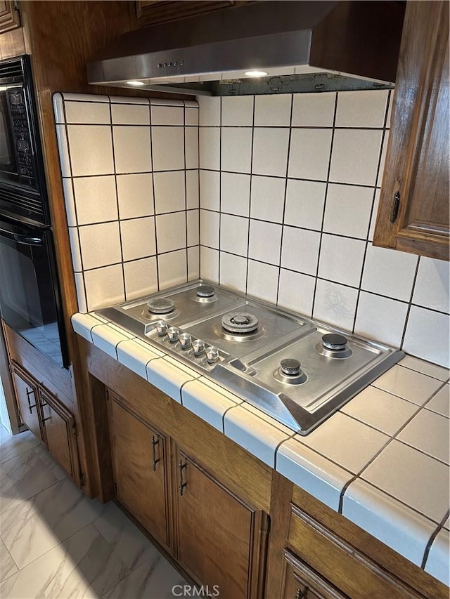 kitchen featuring under cabinet range hood, tile countertops, black appliances, and marble finish floor