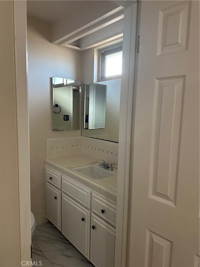 half bathroom with marble finish floor, vanity, and toilet