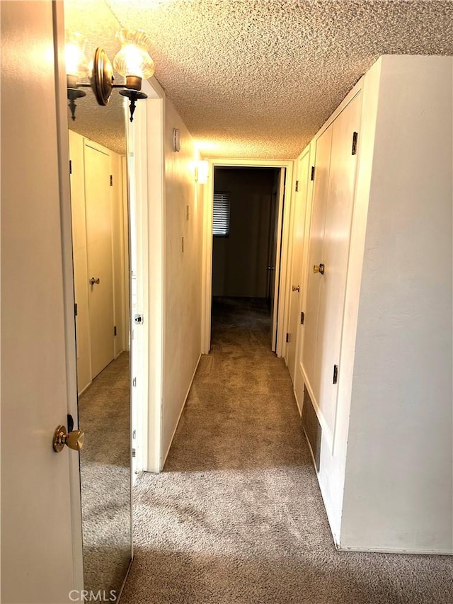 hallway with carpet floors, visible vents, and a textured ceiling