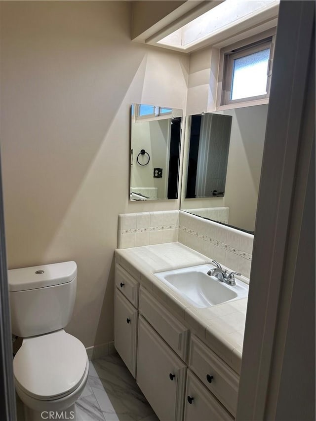 half bath with baseboards, toilet, marble finish floor, vanity, and backsplash