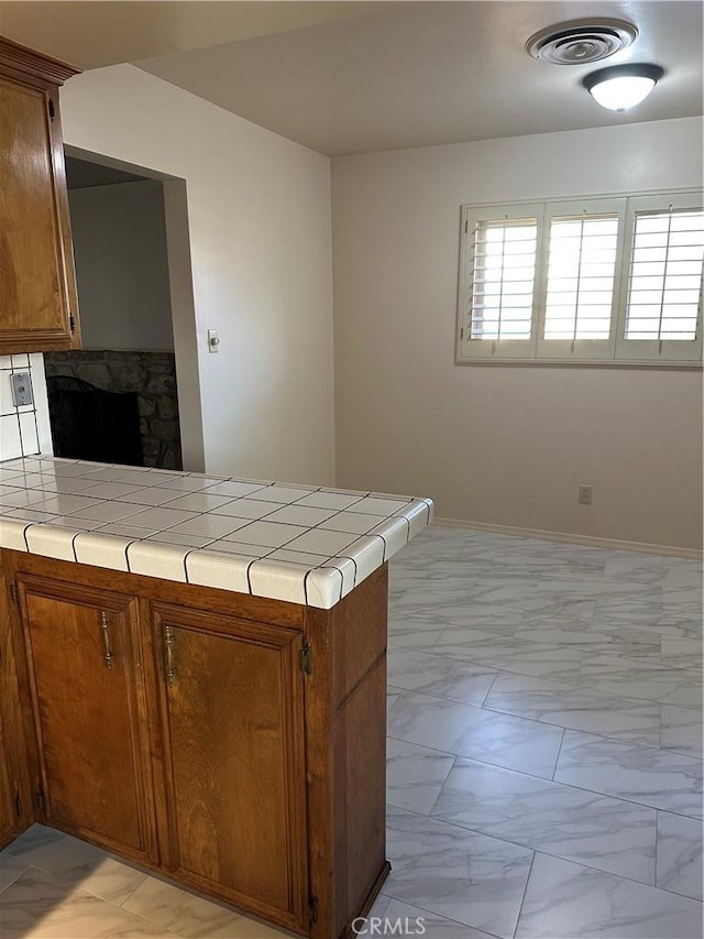 kitchen featuring tile countertops, a peninsula, visible vents, marble finish floor, and brown cabinetry