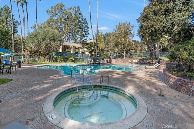 community pool featuring a patio area, fence, and a hot tub