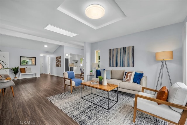 living area featuring vaulted ceiling with skylight, baseboards, and wood finished floors