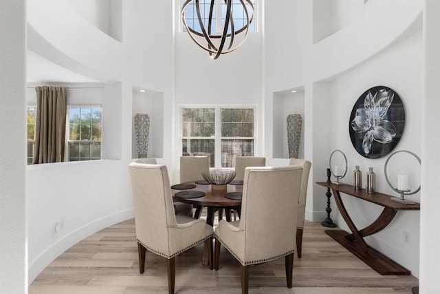 dining area with light wood finished floors, a notable chandelier, a high ceiling, and baseboards