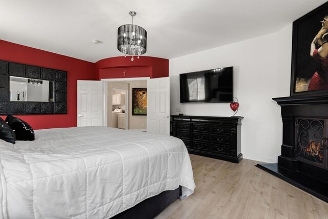 bedroom with a notable chandelier, wood finished floors, baseboards, and a lit fireplace