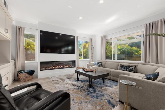 living area featuring a glass covered fireplace, wood finished floors, and recessed lighting