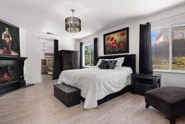 bedroom featuring wood finished floors, visible vents, a lit fireplace, and a chandelier