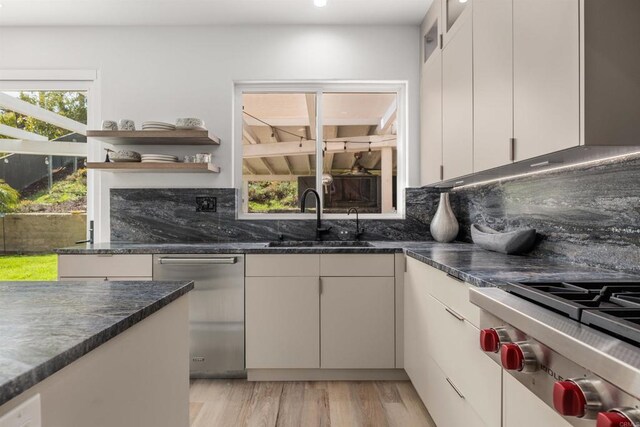 kitchen featuring open shelves, stainless steel appliances, decorative backsplash, a sink, and light wood-type flooring