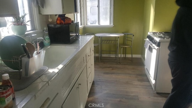 kitchen with black microwave, wood finished floors, white cabinetry, baseboards, and light countertops