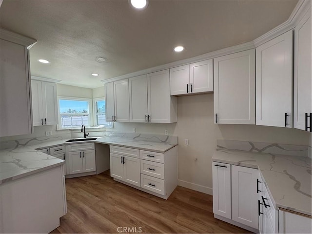 kitchen featuring light stone countertops, light wood finished floors, recessed lighting, a sink, and white cabinets