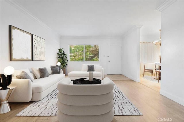 living area featuring ornamental molding, a notable chandelier, light wood-style floors, and baseboards