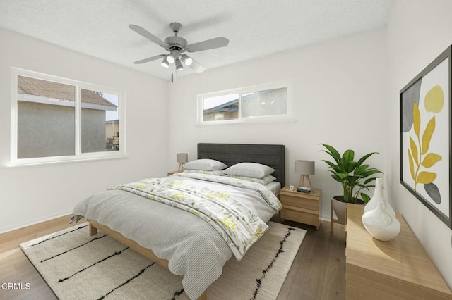 bedroom with a textured ceiling, wood finished floors, a ceiling fan, and baseboards