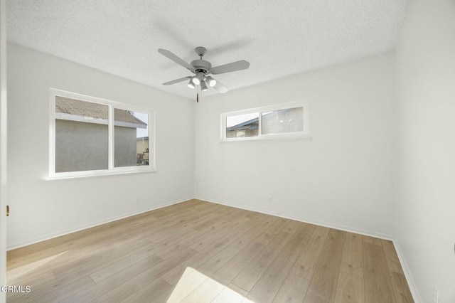 unfurnished room with a textured ceiling, ceiling fan, light wood-type flooring, and baseboards