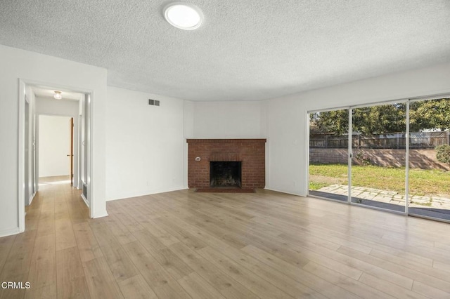 unfurnished living room featuring a brick fireplace, a textured ceiling, baseboards, and wood finished floors