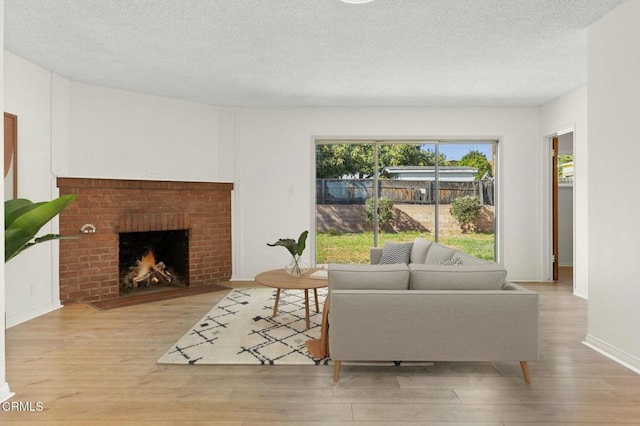 living room featuring a textured ceiling, a brick fireplace, wood finished floors, and baseboards